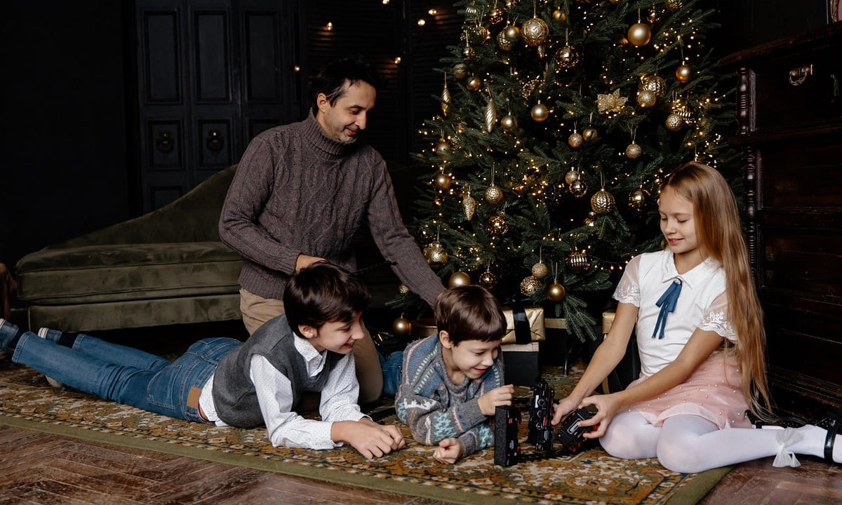 Dad and three kids opening Christmas presents by a lit tree in a cozy living room