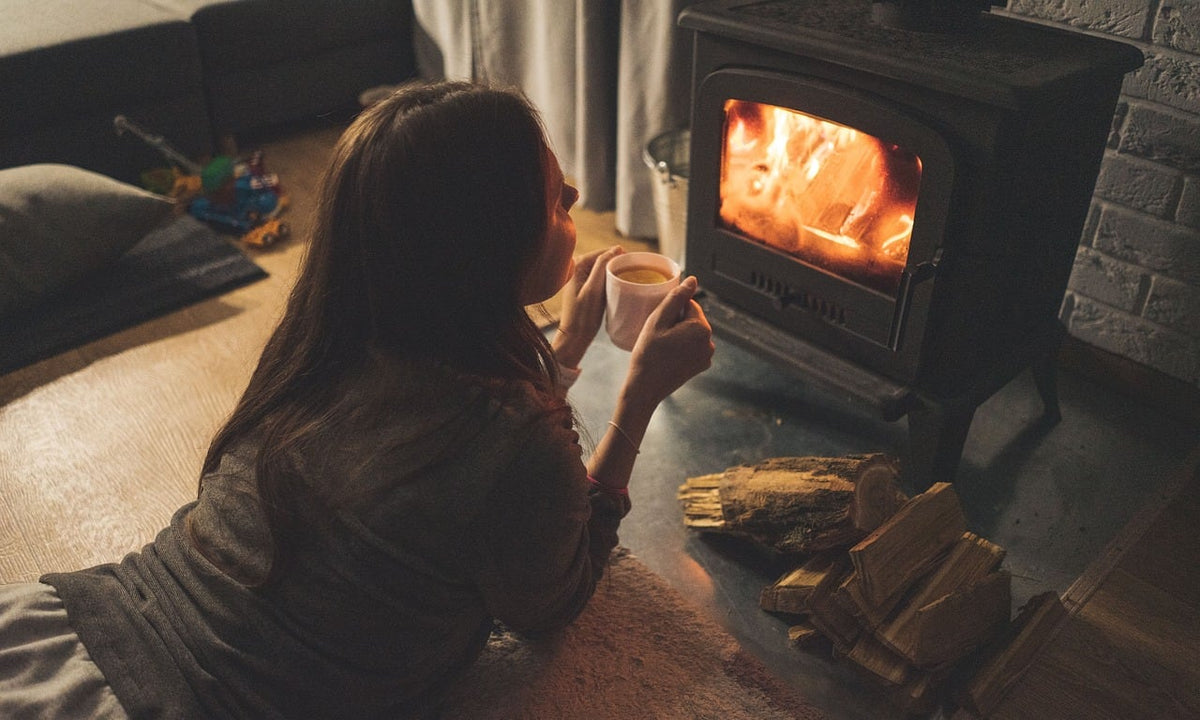 Woman lying on a rug by a wood-burning fireplace holding a warm mug