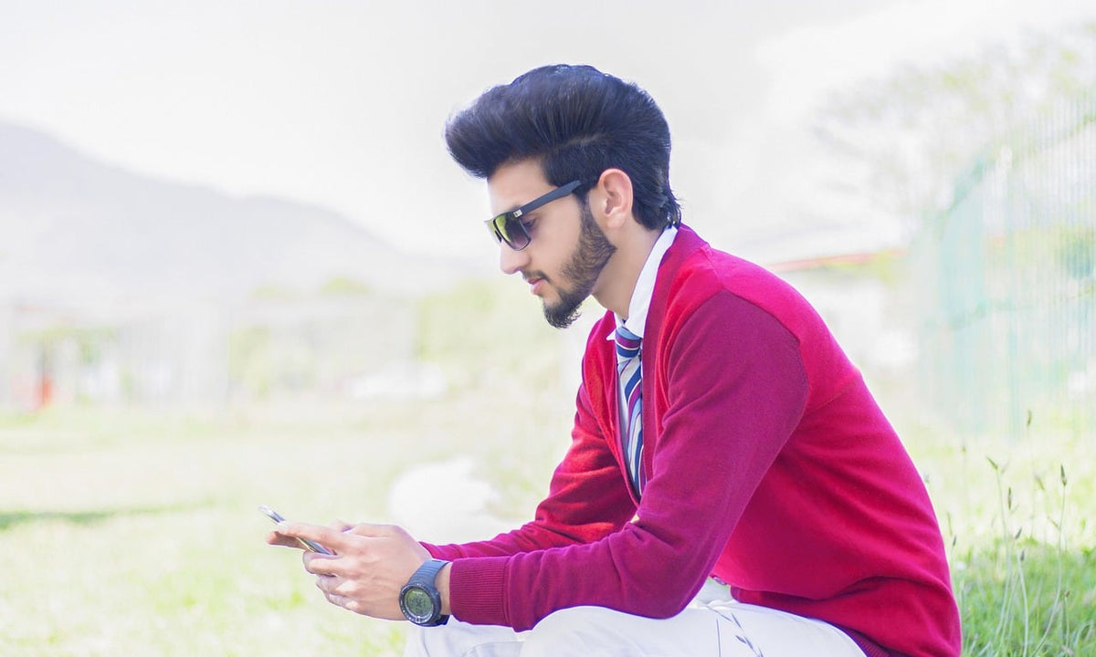 Young man sitting outdoors looking down at his smartphone with his head tipped forward
