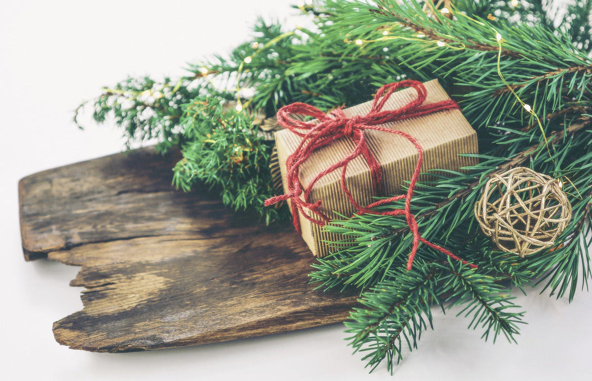 Kraft-paper wrapped gift with red twine on rustic wood with pine branches