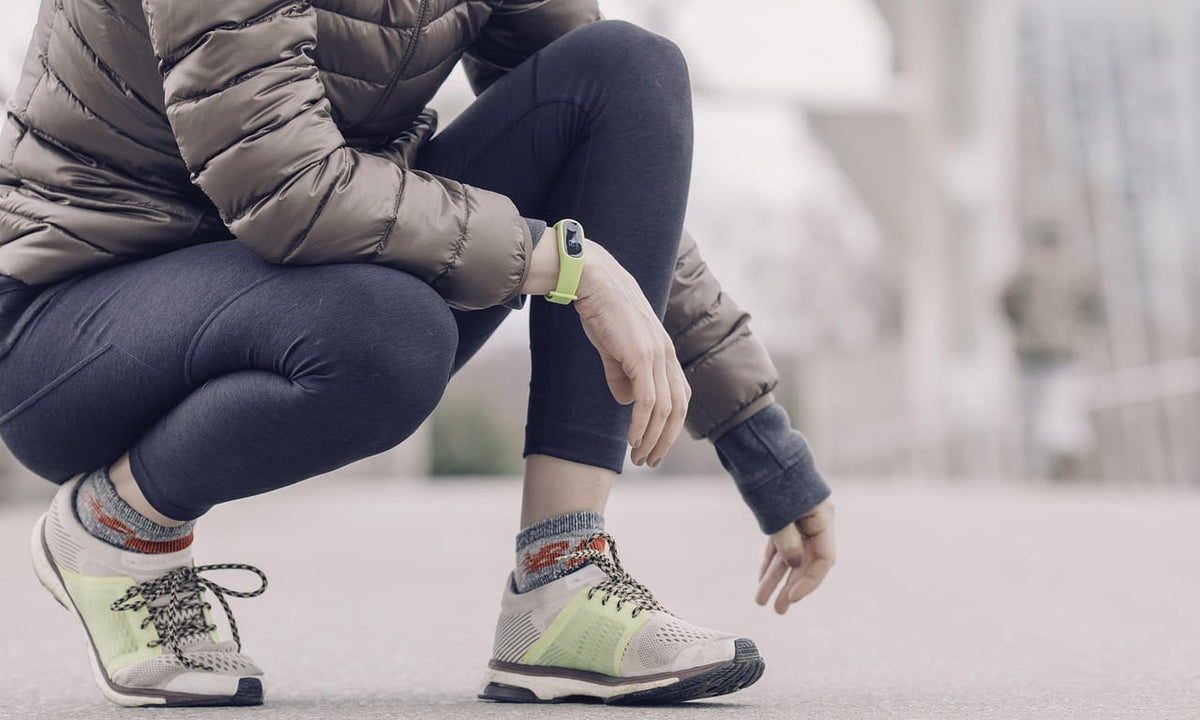 Person in a puffer jacket and leggings crouching on a sidewalk to rest after a walk