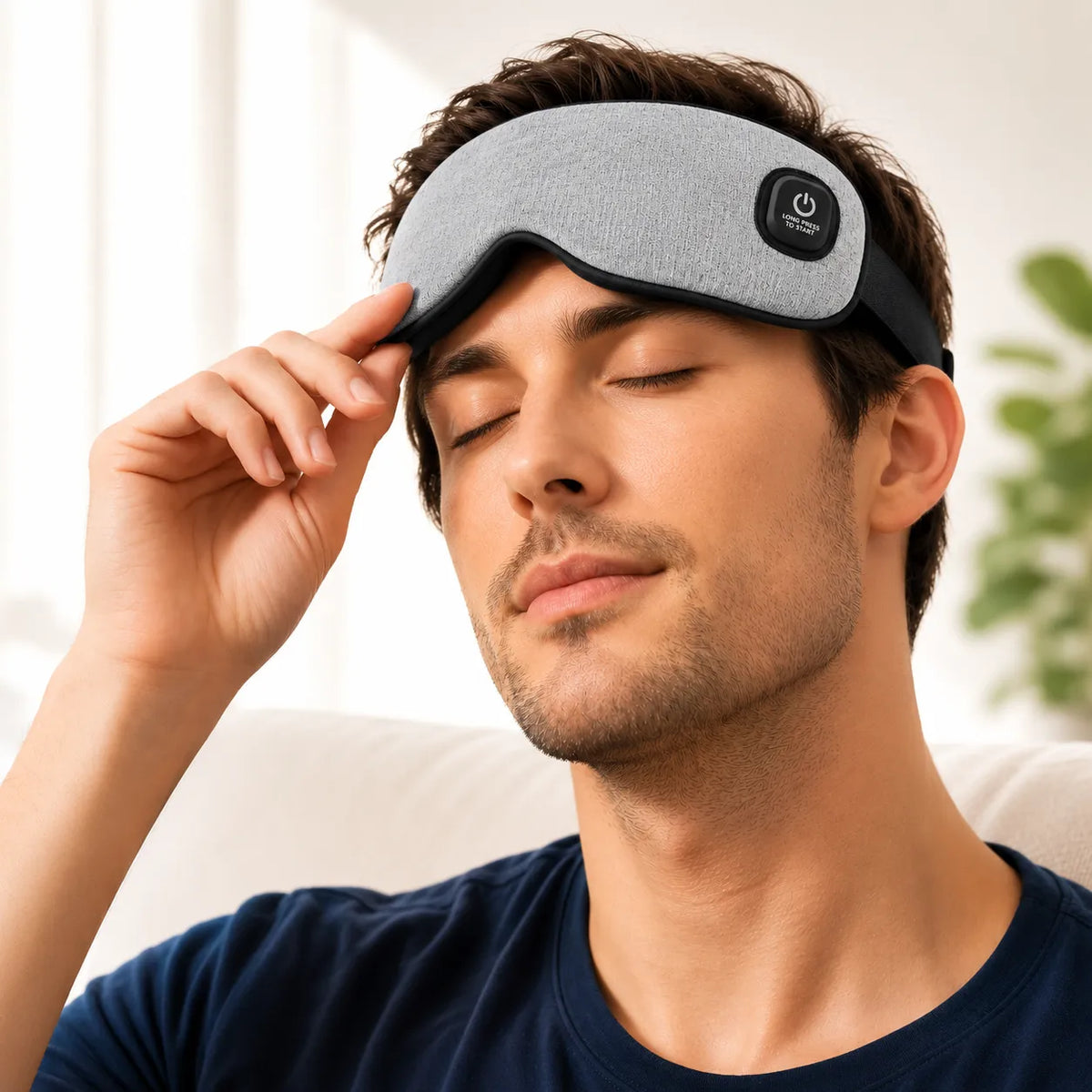 Man relaxing on a sofa with a grey heated eye massager pushed up on his forehead