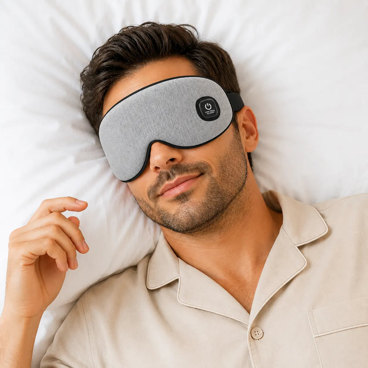 Man lying on a white pillow wearing a grey heated eye massager