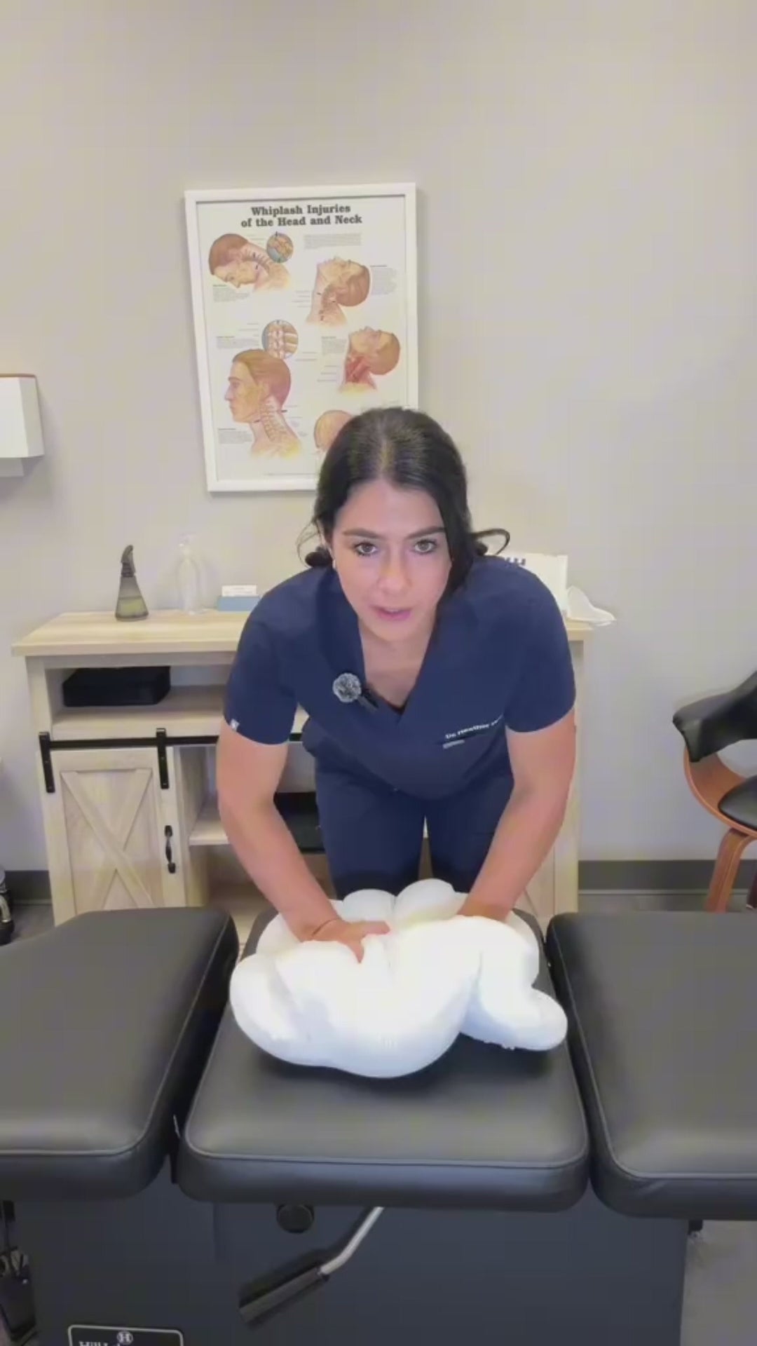 Woman in navy scrubs pressing on a white contoured pillow on a treatment table